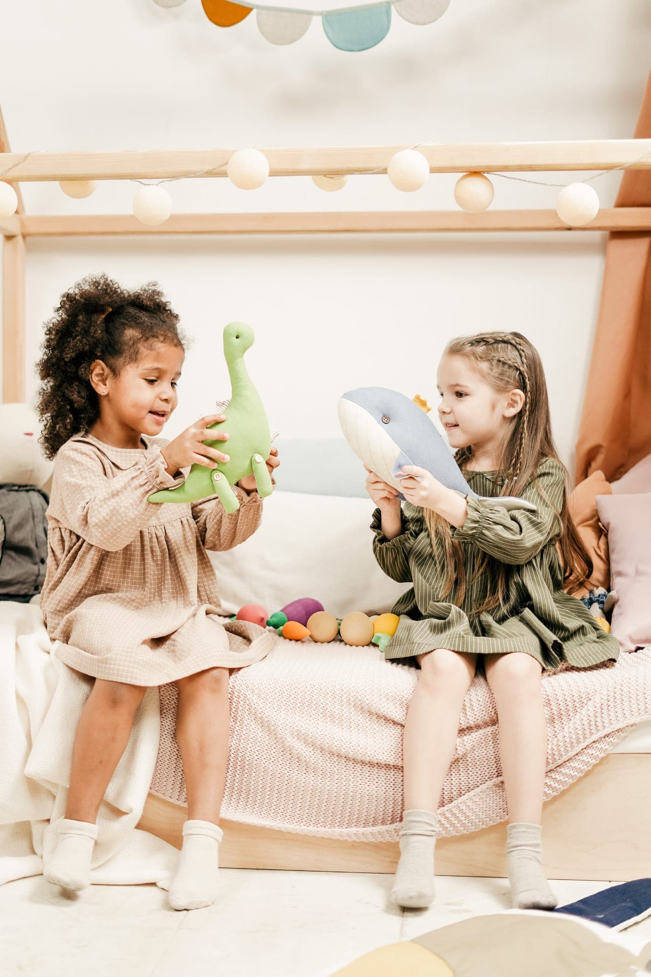 Dos niñas sentadas en una cama juegan con dinosaurios de juguete.