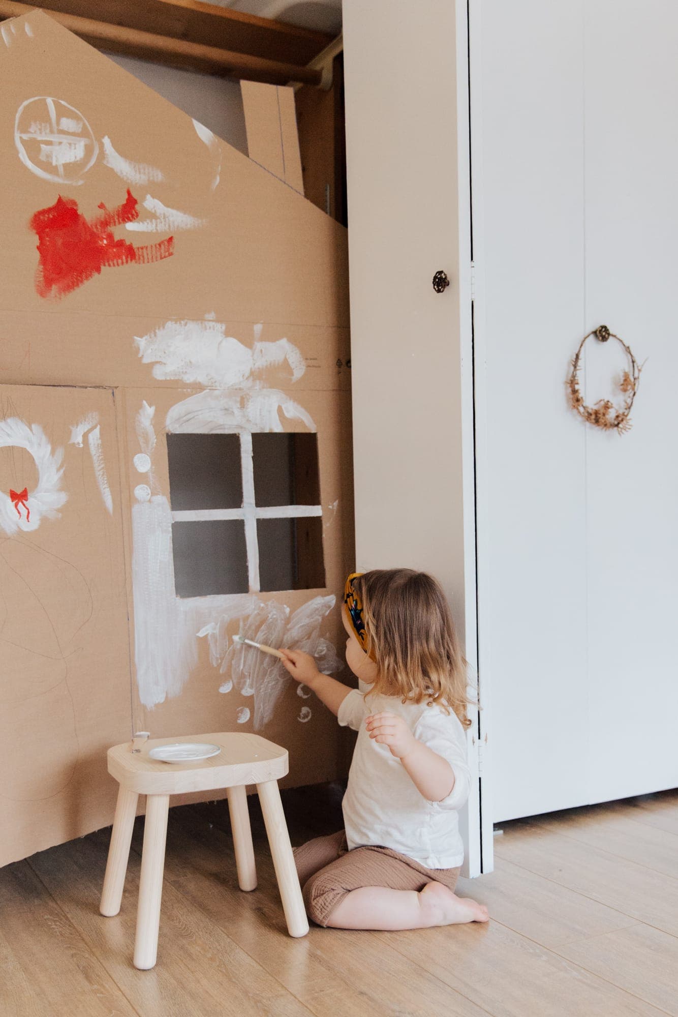 Una niña pinta con pincel una casita de cartón.